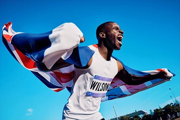 A black male athlete draped in a Union Jack flag running and feeling good about how sleep has impacted his athletic performance.