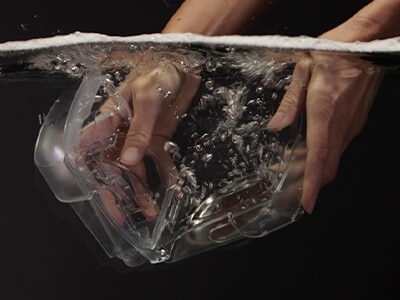 A pair of hands plunging a ResMed CPAP device humidifier tub into some water against a black background