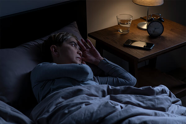 A women lying awake at night with her bedside lamp on looking at her clock because she has insomnia.