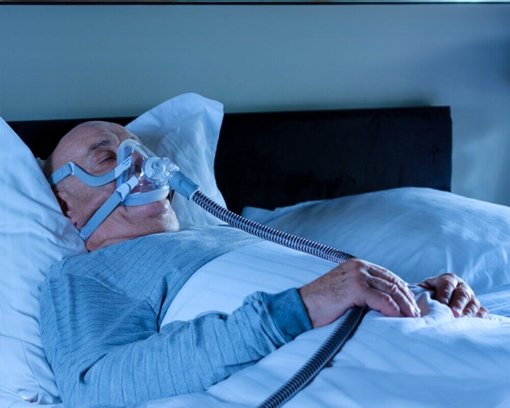 A man sleeping in bed while breathing through a ventilator